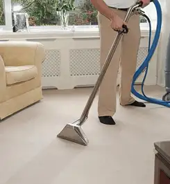 Professional carpet cleaner using a hot-water extraction wand and hose machine in a living room in Dallas, TX.