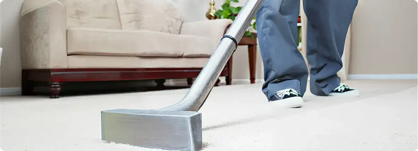 Carpet cleaning technician using a hot-water extraction wand on a light-colored carpet in a living room, Dallas, TX.