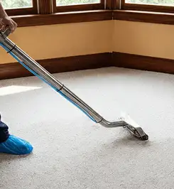 Steam carpet cleaning technician using a hot-water extraction wand on a residential carpet, wearing blue protective shoe covers Dallas, TX.