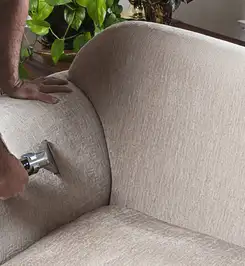 Professional upholstery cleaner deep-cleaning a fabric sofa with a handheld extraction tool and hose Dallas, TX.